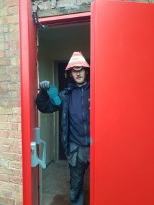 Man posing through a red door holding a large key shaped object