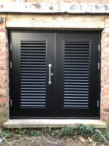 Black Louvered double doors with a pull handle outside a building