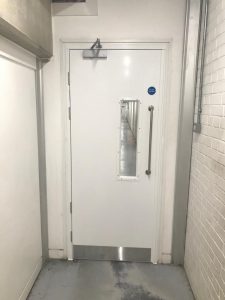 White security door with a window in a white brick room