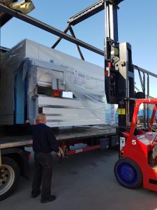 Large Machine on the back of a truck being lifted by a forklift