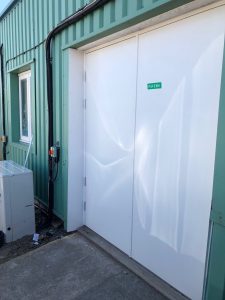 White double security doors outside a green building
