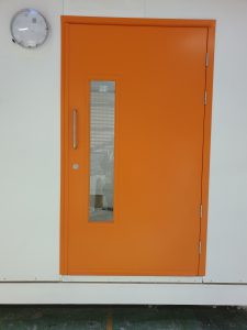 Orange steel door with a window in a white room