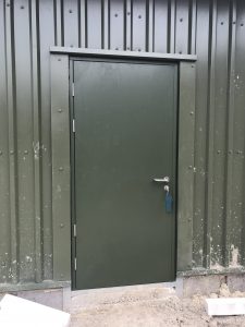 Black steel security door with a silver handle outside a black panelled building