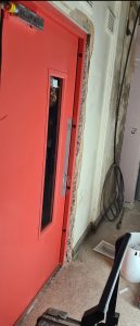 Red security door with a window panel in an unfinished room