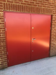 Red double security doors with silver handle and lock surrounded by red brick