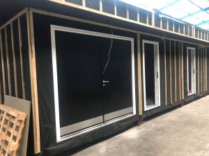 Black double security doors with silver kickplates and handles on an unfinished building