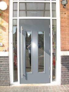 Grey front door with two glass panels and a large vertical pull bar