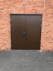 Black double security door with black handle on a red brick wall