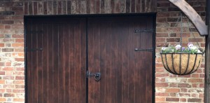 Brown Wooden Double Doors with black handle and hinges with a hanging flower basket in front