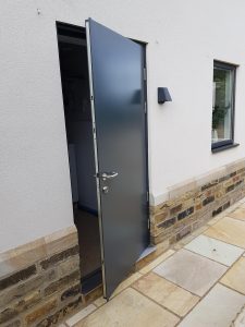 Black steel door partially open leading into a white building