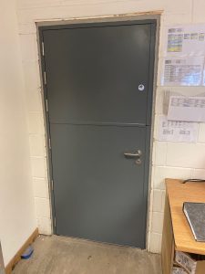 Grey security door with a silver handle in a white cinderblock room