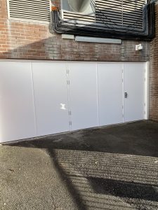 White folding security doors with a silver handle with a security camera and air conditioning unit above