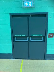 Double grey fire doors with push bars to open in a green room