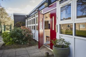 Red double steel doors with one open on a white builidng
