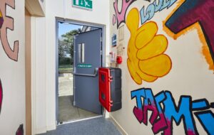 Open grey fire exit door with graffiti inside a building