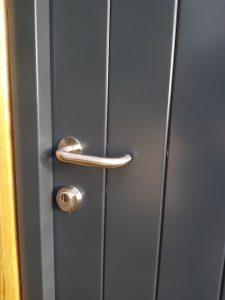 Closeup of a grooved black door with a sliver handle and lock