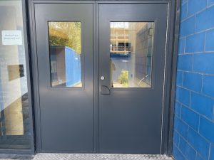 Black double doors with glass panes next to a blue brick wall