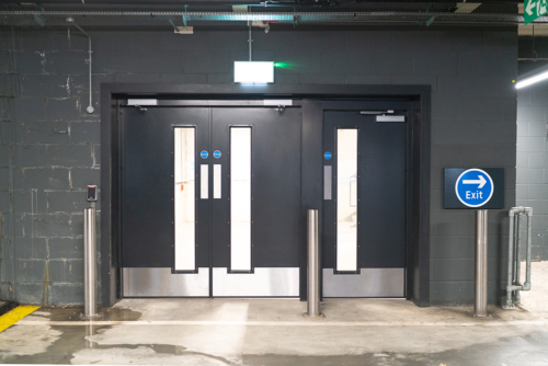 Metador's Safeguard steel doors installed in a public parking garage, being used as personnel fire doors leading to the stairwell. Featuring a double and single configuration, in a dark grey powdercoat with kick plates to the bottom of the doorsets.